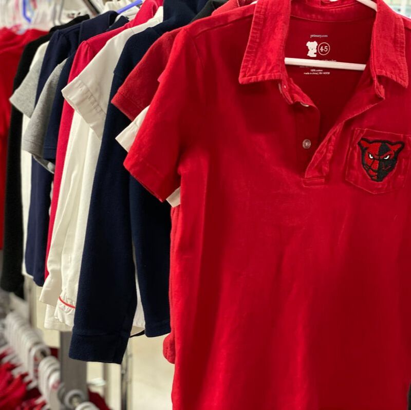 Red, Navy blue, White, and Gray uniform polos are hanging on clothing racks. There is emphasis on a red polo shirt that contains a Petal panther logo.
